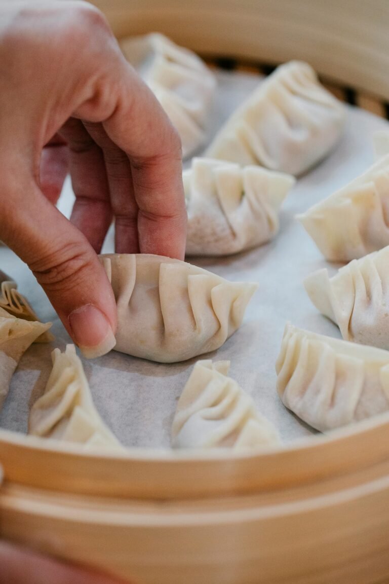 High angle of anonymous crop cook touching delicious dumplings in soft focus while arranging in bamboo steamer
